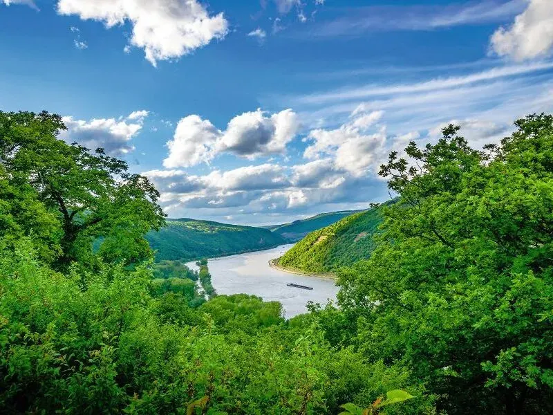 Eine malerische Flusslandschaft mit bewaldeten Hügeln und blauem Himmel.
