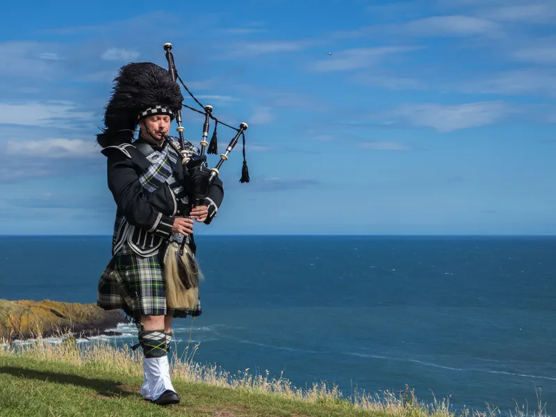 Traditioneller schottischer Dudelsackspieler in vollständiger Tracht mit dem Meer im Hintergrund.