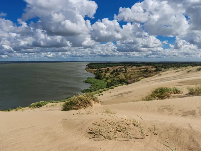 Küstenlandschaft mit Sanddünen und bewölktem Himmel am Meer.
