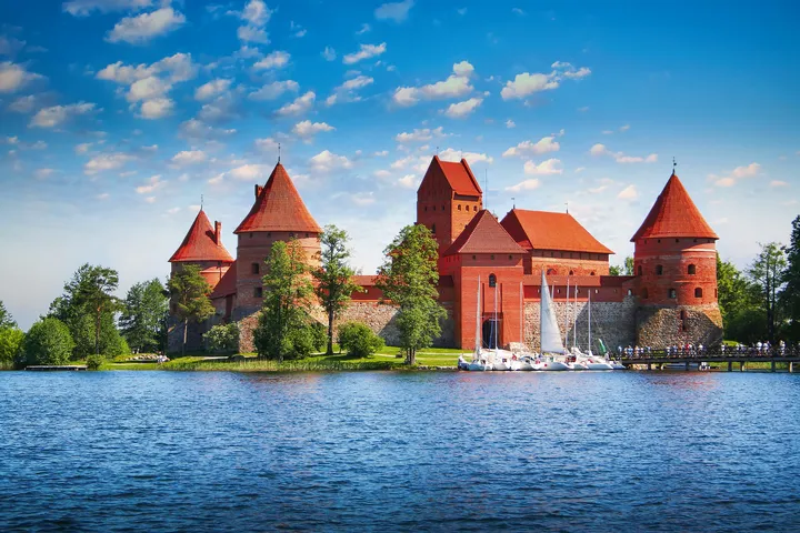 Rote Backsteinburg am Seeufer mit Segelbooten und bewölktem Himmel.