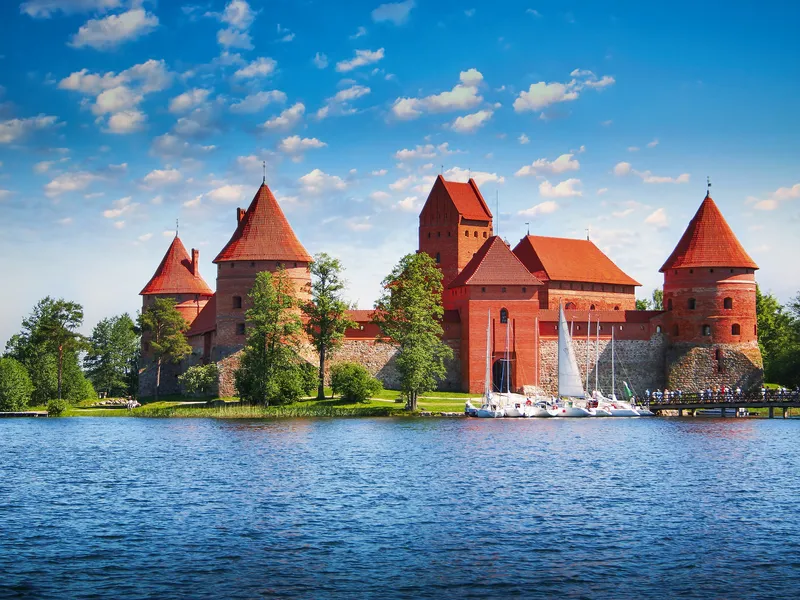 Rote Backsteinburg am Seeufer mit Segelbooten und bewölktem Himmel.