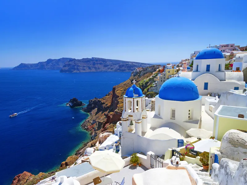 Weiße Gebäude mit blauen Kuppeln auf Santorini, Meer im Hintergrund.