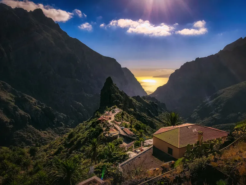 Gebirgspanorama mit Haus, steilen Felsen und Sonnenuntergang im Hintergrund