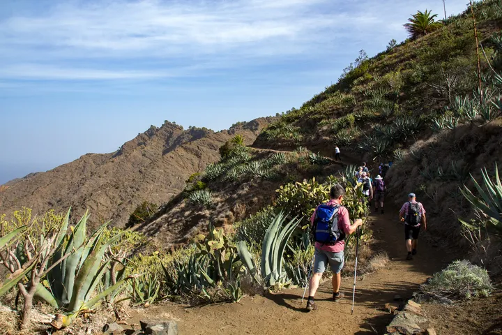 © Tanja Wilbertz - stock.adobe.com Wanderer auf einem Pfad im Norden von La Gomera bei Hermigua, umgeben von Bergen und Vegetation.
