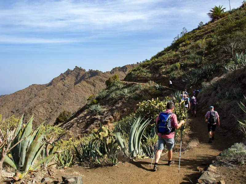 Wanderer auf einem Pfad im Norden von La Gomera bei Hermigua, umgeben von Bergen und Vegetation.