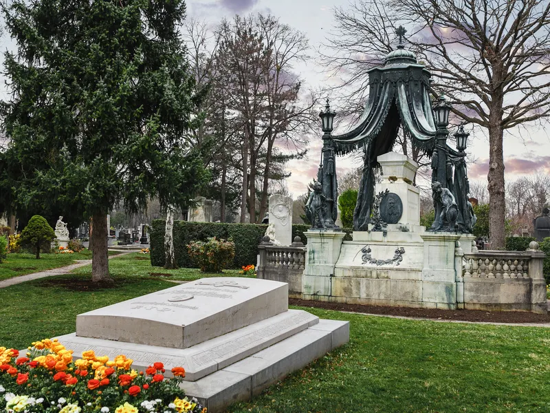Ein Grabmal auf dem Wiener Zentralfriedhof, umgeben von Bäumen und Blumenbeeten im Frühling.