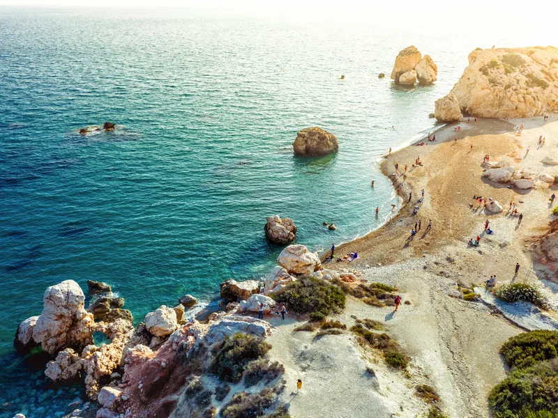 Küste mit Felsen und klarem Meerwasser, Menschen genießen den Strand.