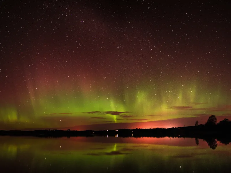 Aurora Borealis über dem Loch of Skene in Aberdeenshire, Schottland, mit bunten Polarlichtern am Nachthimmel und ihrer Spiegelung im Wasser.