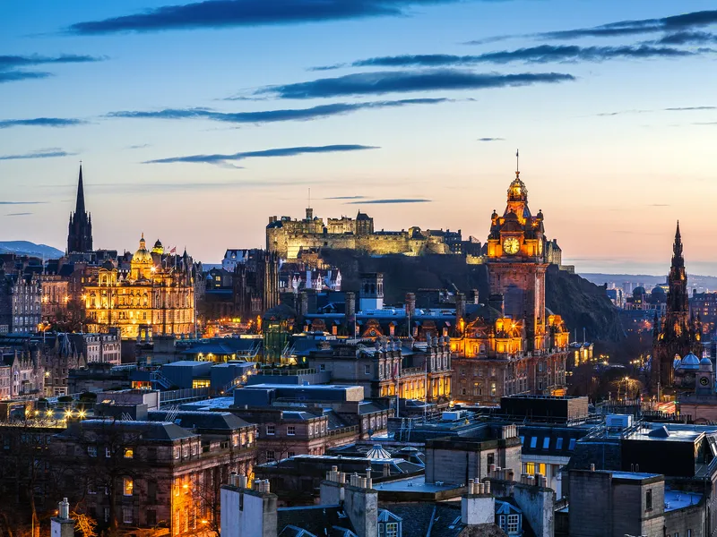 Blick auf Edinburgh zur Dämmerung im Winter, beleuchtete Stadt mit der Burg im Hintergrund.