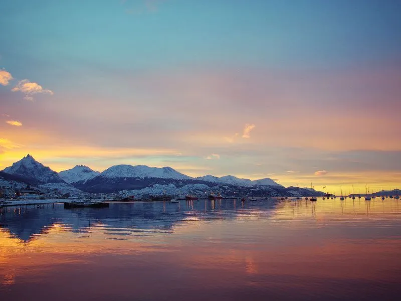Sonnenuntergang über einem ruhigen See mit schneebedeckten Bergen im Hintergrund und reflektierendem Wasser.