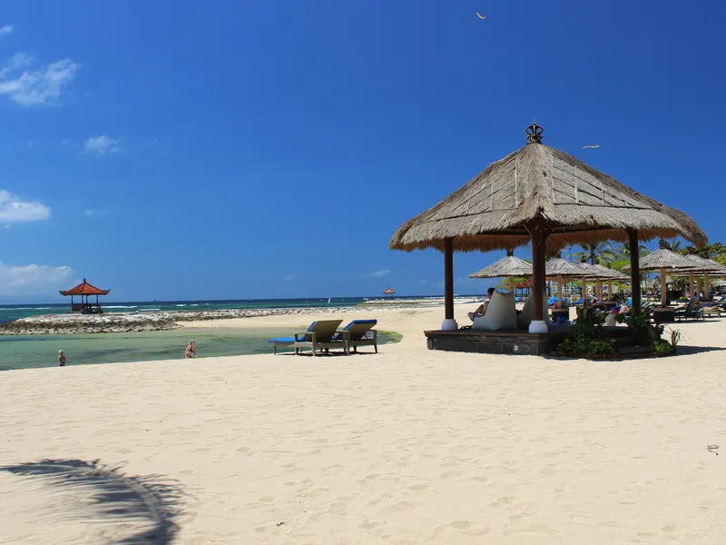 Strand mit Sonnenschirmen und Liegen, blauer Himmel, ruhiges Meer.