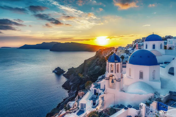 Kuppelkirchen und Sonnenuntergang über Santorini, Griechenland, mit Blick auf das Meer