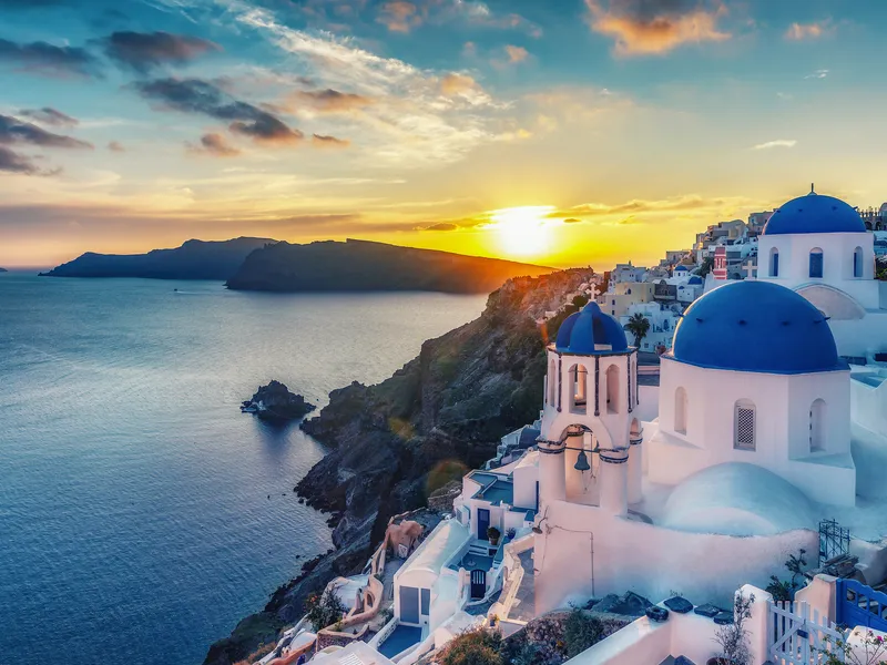Kuppelkirchen und Sonnenuntergang über Santorini, Griechenland, mit Blick auf das Meer
