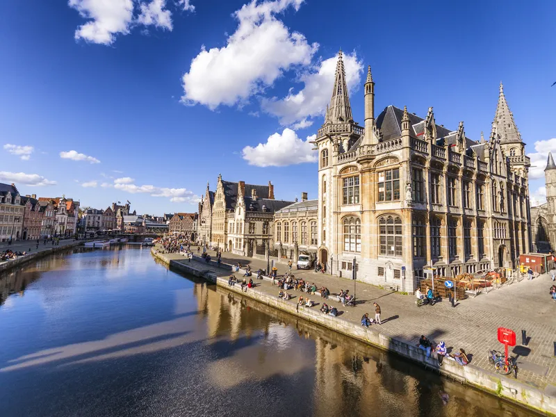 Blick auf die Stadt Gent in Belgien mit der Sint-Niklaaskerk und dem Fluss Leie bei sonnigem Wetter.