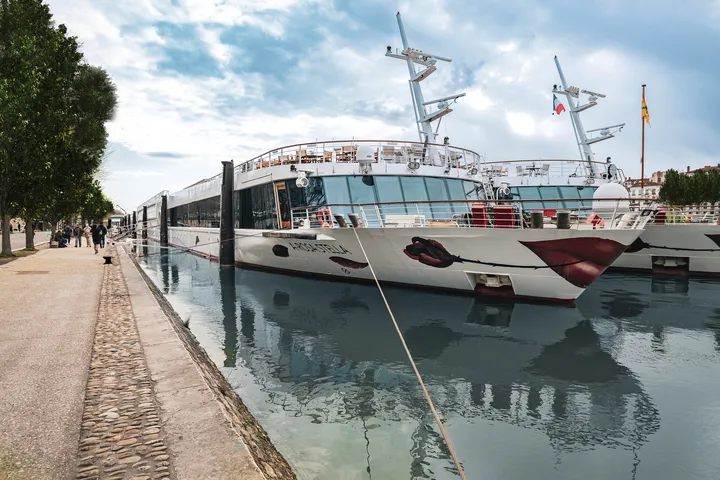 Flusskreuzfahrtschiff im Hafen, reflektiert im Wasser.