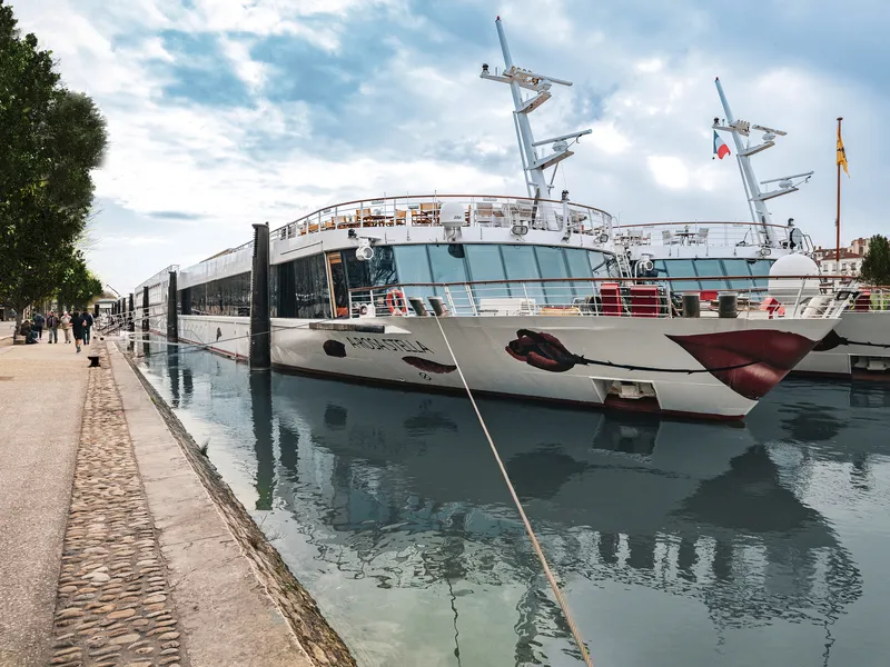 Flusskreuzfahrtschiff im Hafen, reflektiert im Wasser.