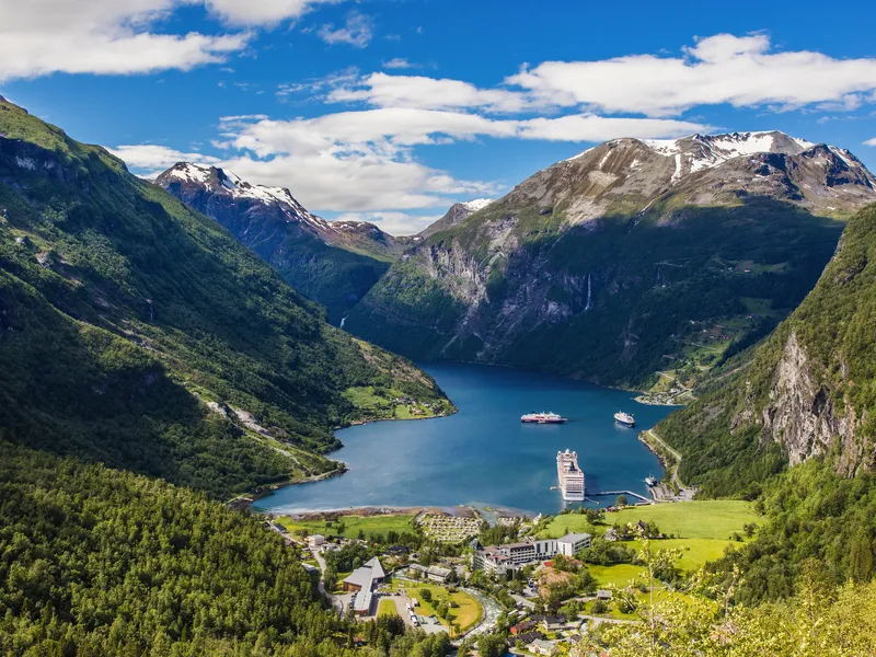 Blick auf den Geirangerfjord mit Bergen und einem Kreuzfahrtschiff im Wasser.