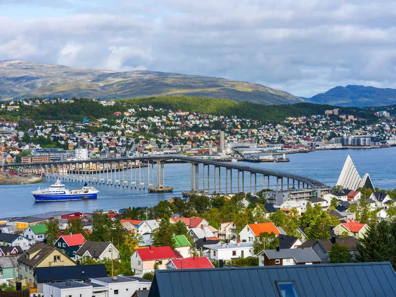Küstenstadt mit Brücke, Schiff und Bergen im Hintergrund.