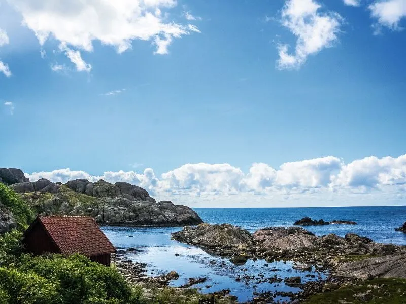 Kleine Hütte am felsigen Meerufer mit blauem Himmel und Wolken.