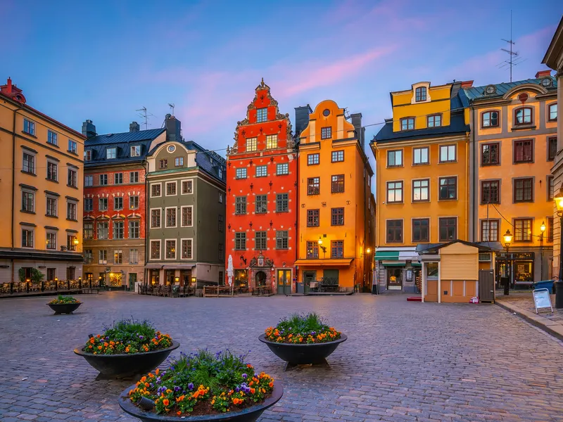 Ein Platz mit historisch bunten Gebäuden und Blumenkübeln bei Sonnenuntergang.