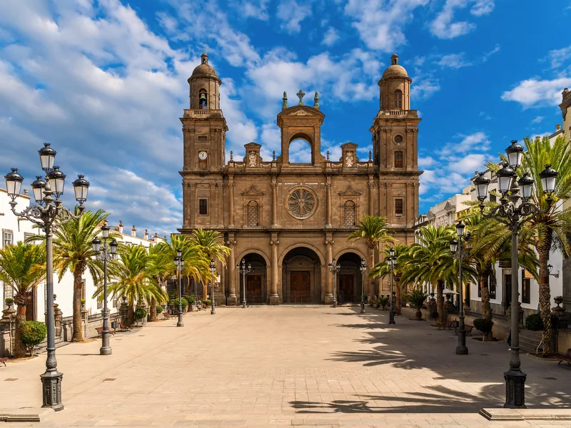 Kathedrale mit Türmen und Palmen auf einem sonnigen Platz.