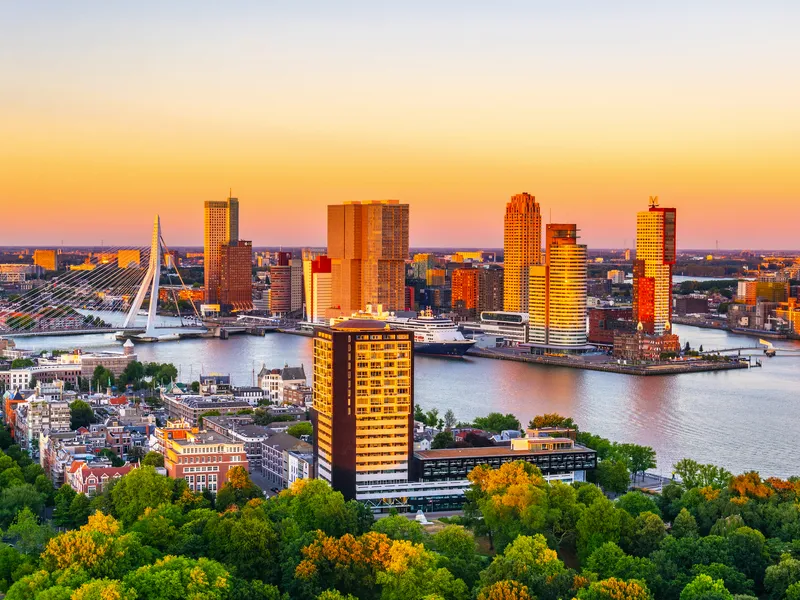 Skyline von Rotterdam bei Sonnenuntergang mit Erasmusbrücke und Hochhäusern am Wasser.