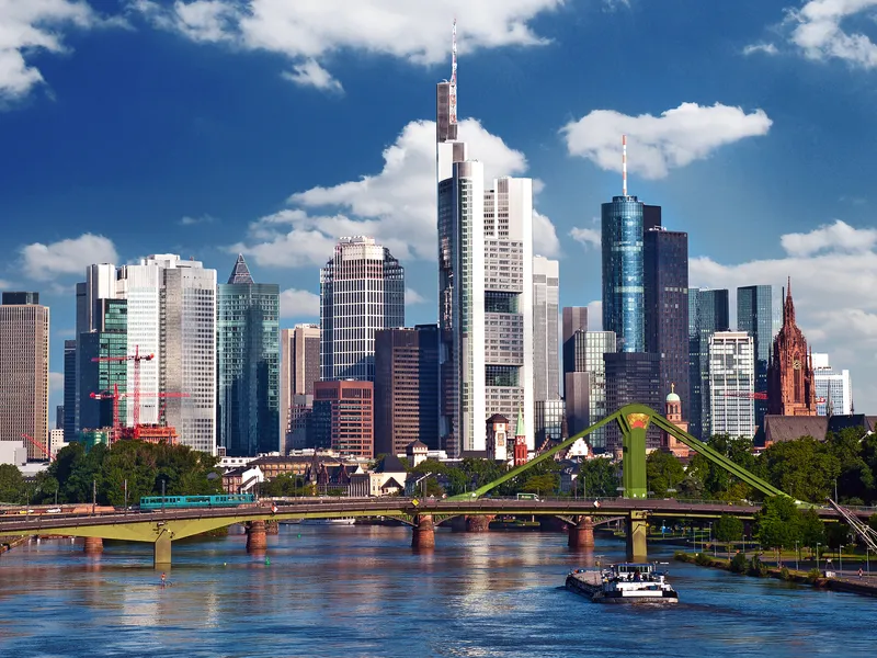 Skyline von Frankfurt am Main mit Wolkenkratzern und Fluss im Vordergrund.