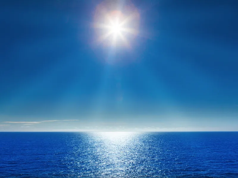 Klares Meer mit strahlendem Sonnenschein am blauen Himmel.