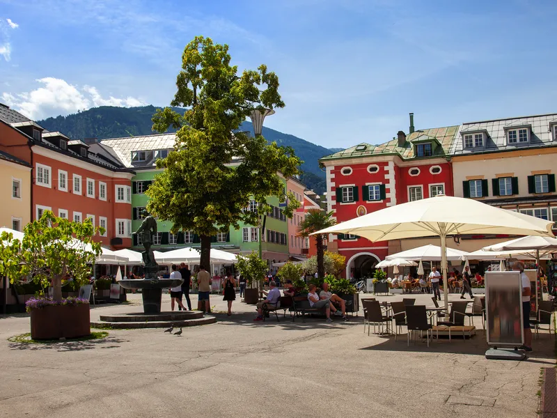 Städtischer Platz mit bunten Gebäuden, Cafés und Menschen bei sonnigem Wetter.