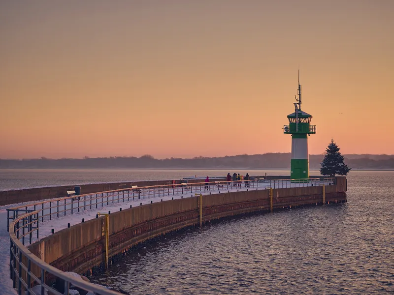 Leuchtturm bei Sonnenuntergang an einem schneebedeckten Steg.