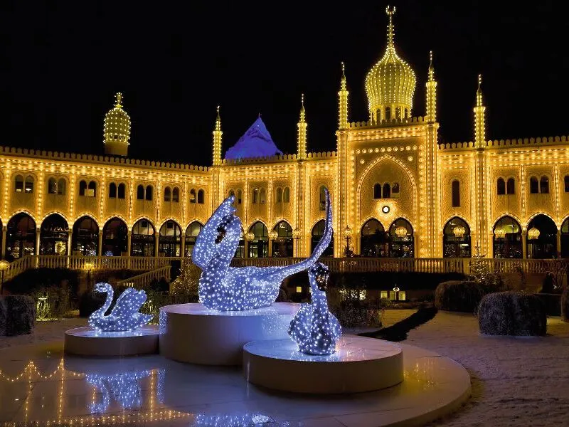 Nachts beleuchteter orientalischer Palast mit funkelnden Lichtskulpturen im Vordergrund.
