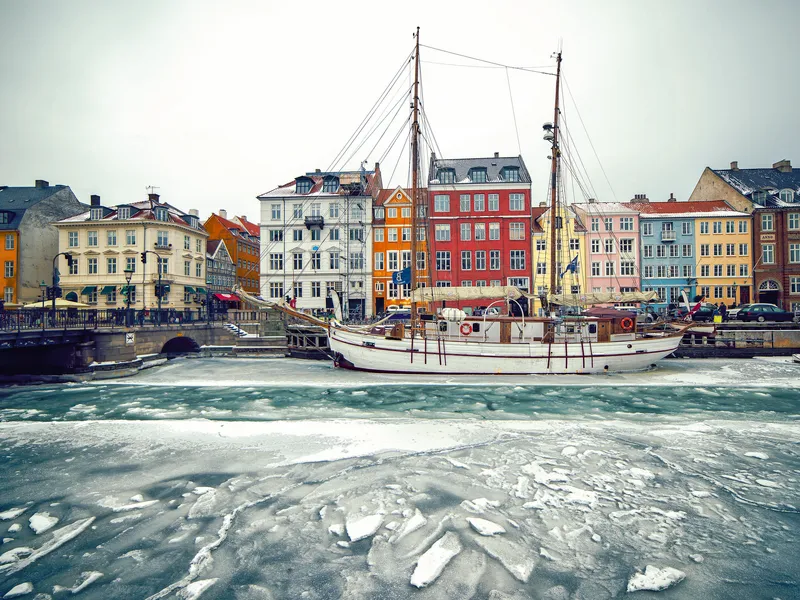 Ein Schiff im gefrorenen Wasser vor einer Reihe bunter Gebäude in einer alten europäischen Stadt.