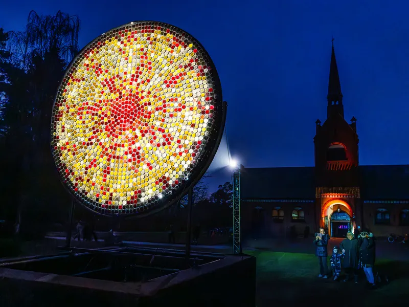 Leuchtende Kunstinstallation im Freien bei Nacht vor einem beleuchteten Gebäude.