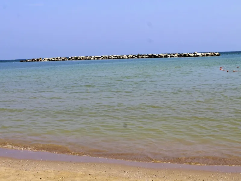 Strand mit ruhigem Meer und Steinbarriere am Horizont