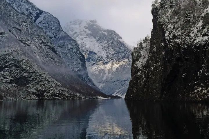 Eine schneebedeckte Berglandschaft spiegelt sich in einem ruhigen Gewässer.