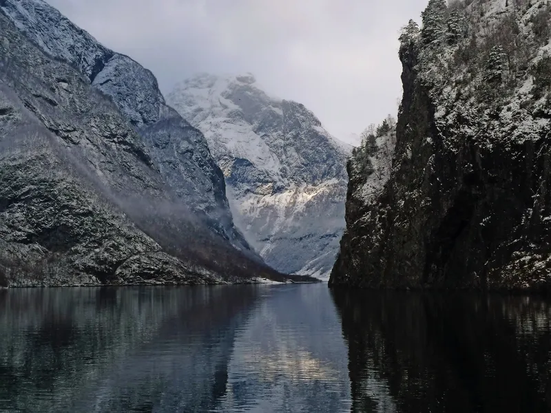 Eine schneebedeckte Berglandschaft spiegelt sich in einem ruhigen Gewässer.