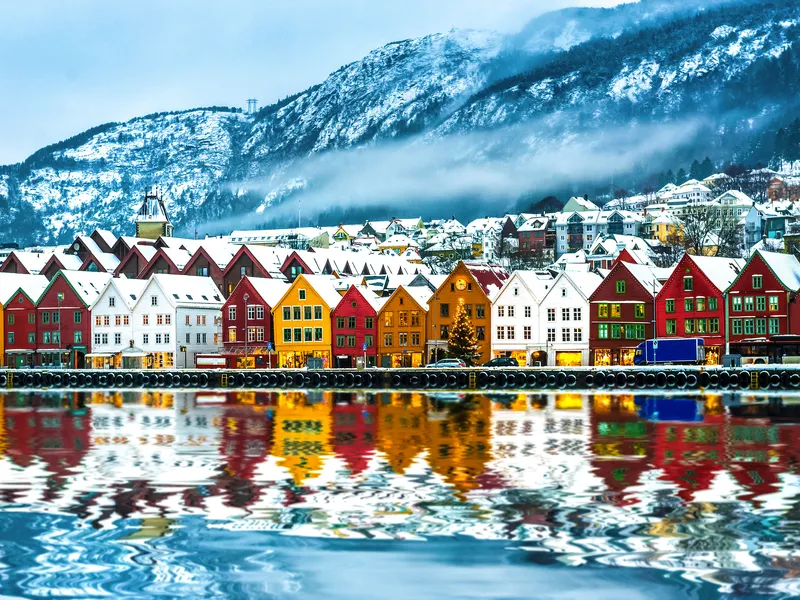 Bunte Häuserzeile in Bergen, Norwegen, mit Schneebedeckten Bergen im Hintergrund.