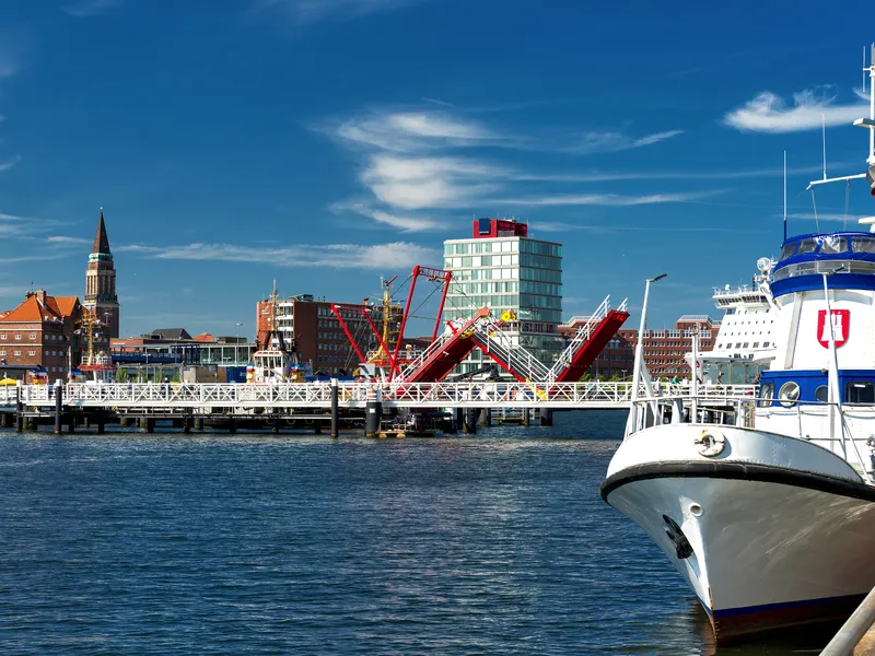 Hafenansicht mit Boot und Stadtpromenade unter blauem Himmel