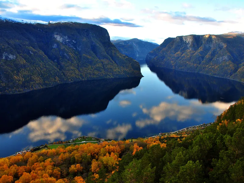 Blick auf einen Fjord mit bewaldeten Hügeln und reflektierendem Wasser.