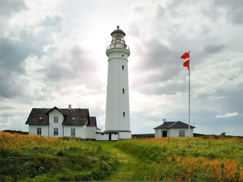 Leuchtturm neben einem Haus auf einer Wiese unter bewölktem Himmel.