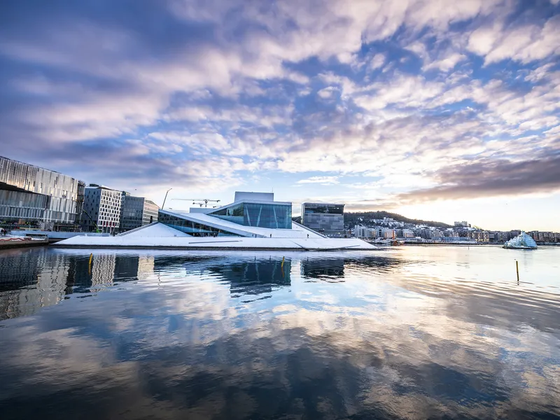 Opernhaus in Oslo, reflektiert im Wasser, mit blauem Himmel und Wolken.