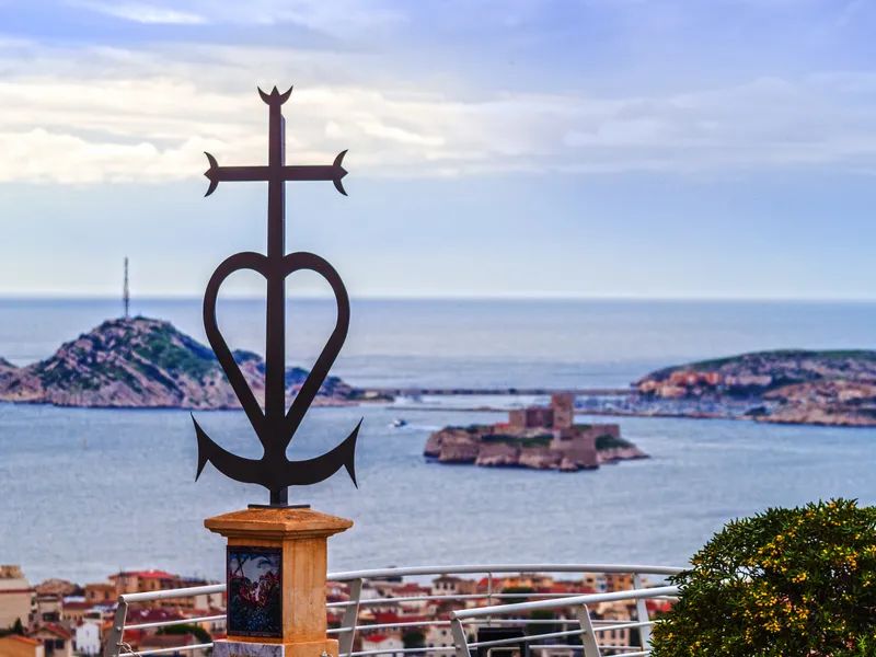 Kunstvolles Kreuz überblickt Stadt am Meer mit Inseln im Hintergrund.