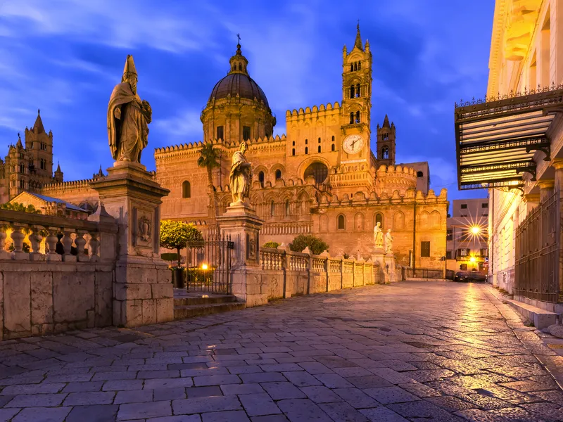 Kathedrale von Palermo bei Dämmerung, umgeben von Statuen und historischem Gebäude.