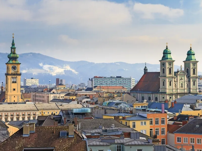 Stadtpanorama mit Kirchtürmen und Bergen im Hintergrund.