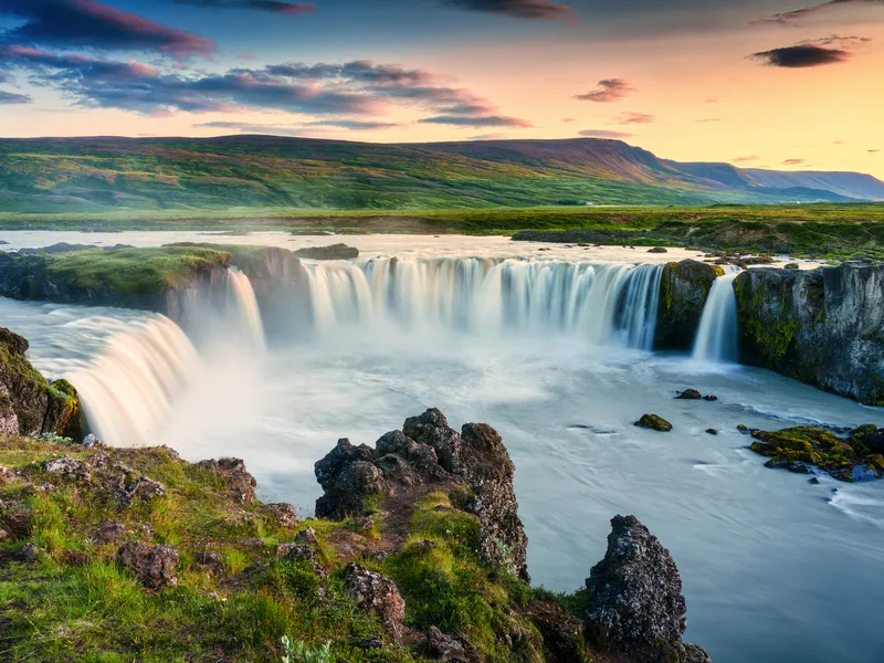 Wasserfall in einer grünen Landschaft bei Sonnenuntergang.