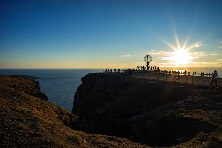 Klippenlandschaft mit Globus-Skulptur und Sonnenuntergang am Horizont.