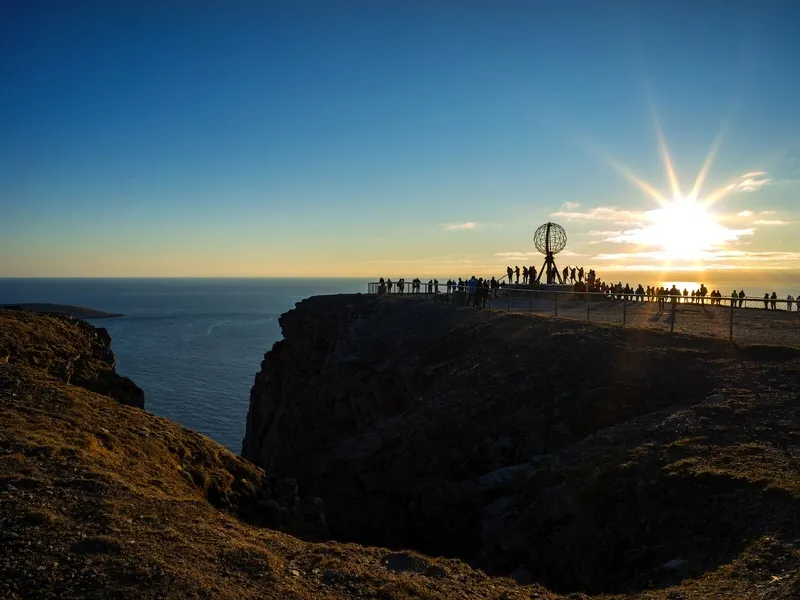 Klippenlandschaft mit Globus-Skulptur und Sonnenuntergang am Horizont.