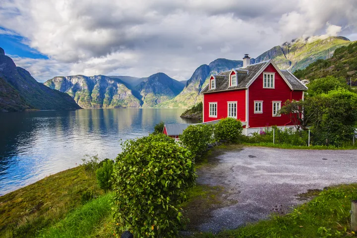 © NataliaKabliuk.com Rotes Haus am Faleidfjord in Olden, Norwegen, umgeben von beeindruckender Fjordlandschaft.