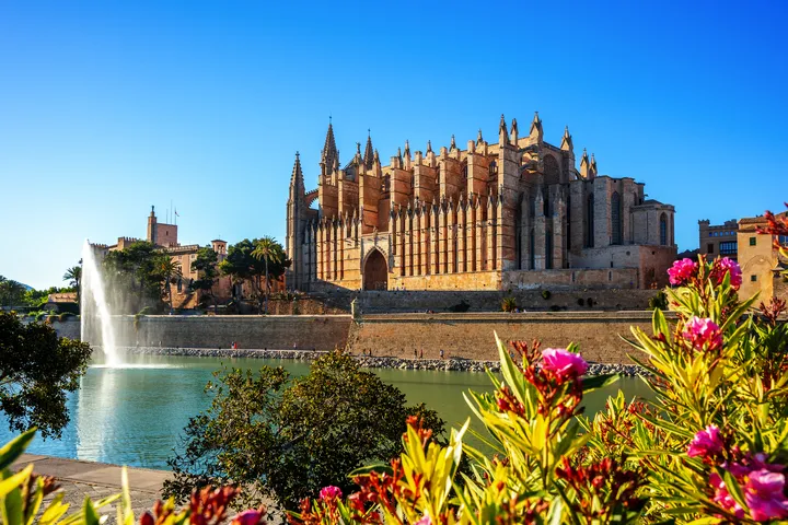 © Sina Ettmer - stock.adobe.com Kathedrale von Palma de Mallorca mit einer blühenden Umgebung und einem See im Vordergrund.