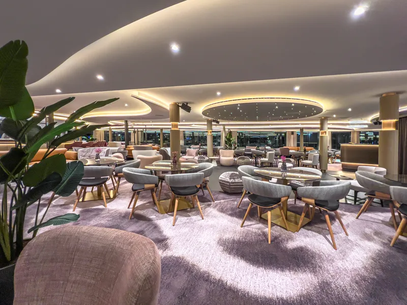 Moderne Lounge mit grauen Sesseln, runden Tischen und Pflanzen.